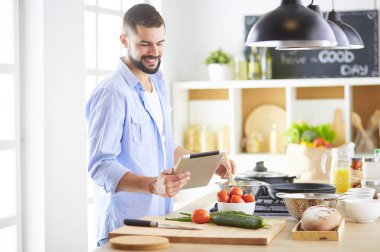 Dijital tablet ve yemek pişirme tarifine uyan bir adam evdeki mutfakta lezzetli ve sağlıklı yemekler pişiriyor.