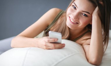 Güzel bir kadın beyaz bir kanepede bir fincan kahveyle dinleniyor.