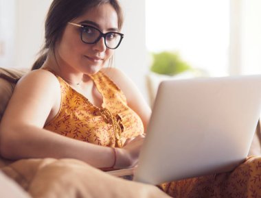 Evde dizüstü bilgisayar üzerinde çalışan kanepede oturan genç kadın