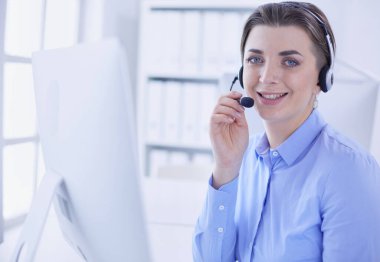 Ofisinde kulaklık takmış, telefon operatörü olarak çalışan ciddi ve güzel bir genç kadın.