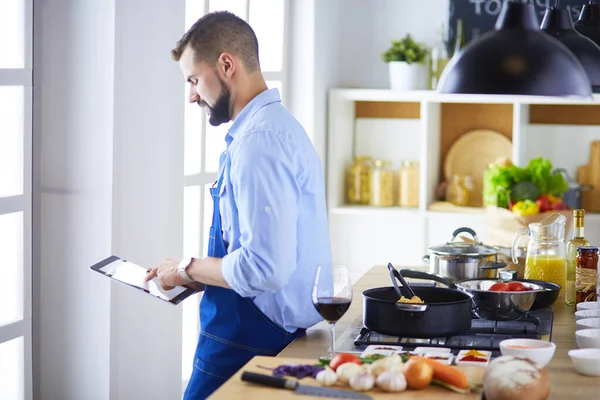 Hombre siguiendo la receta en la tableta digital y cocinar comida sabrosa y saludable en la cocina en casa —  Fotos de Stock