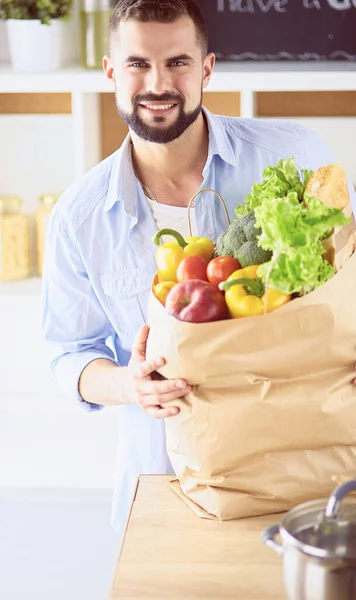 Άντρας που κρατάει χάρτινη σακούλα γεμάτη ψώνια στο φόντο της κουζίνας. Αγορές και υγιεινή διατροφή έννοια — Φωτογραφία Αρχείου