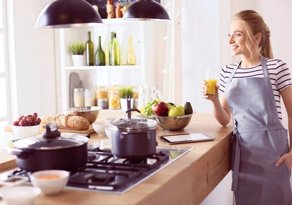 Atractiva mujer sosteniendo un vaso de jugo de naranja mientras está de pie en la cocina —  Fotos de Stock