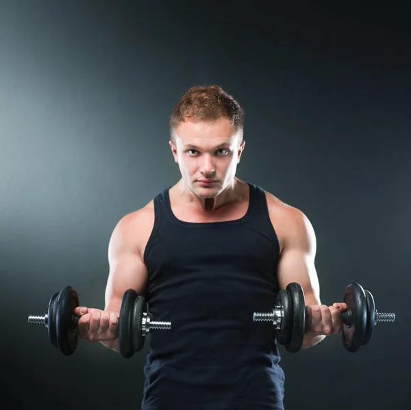 Nahaufnahme eines muskulösen jungen Mannes, der Gewichte auf dunklem Hintergrund stemmt — Stockfoto