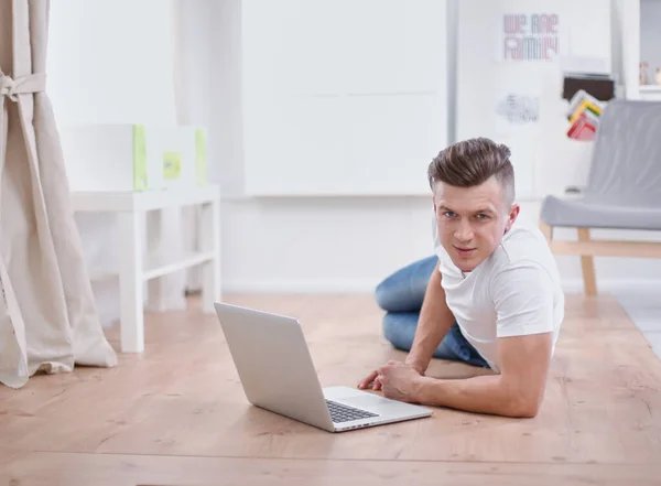 Yakışıklı genç adam dizüstü bilgisayarda oturuyor ve çalışıyor. — Stok fotoğraf