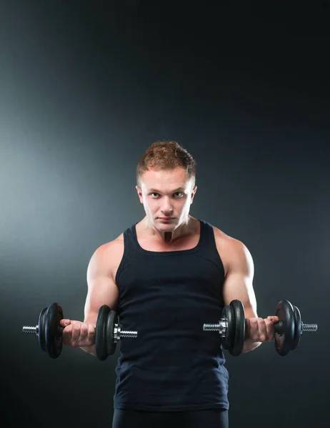 Closeup of a muscular young man lifting weights on dark background — Stock Photo, Image