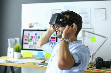 Genç erkek yazılım programcısı ofiste üç boyutlu sanal gerçeklik gözlükleriyle yeni bir uygulama test ediyor..