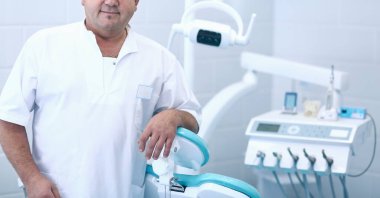 Diş kliniğinde duran gülümseyen bir dişçinin portresi.