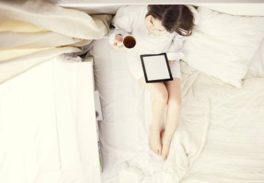 Sabahları yatakta otururken tablet kullanan ve kahve içen kadın portresi