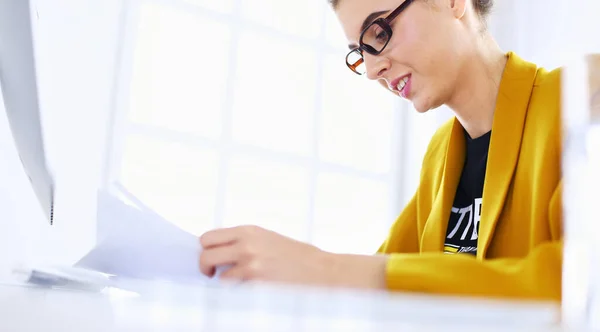 Hermosa joven mujer de negocios haciendo un poco de papeleo mientras está sentado en el escritorio de la oficina delante de la computadora portátil —  Fotos de Stock