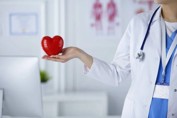 Kvinnelig lege med stetoskop som holder hjertet, med lys bakgrunn – stockfoto