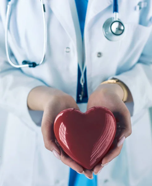 Medico femminile con stetoscopio che tiene il cuore, su sfondo chiaro — Foto Stock