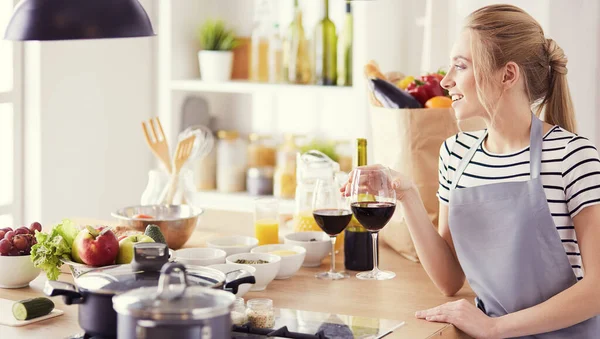 Mujer bonita bebiendo un poco de vino en casa en la cocina —  Fotos de Stock