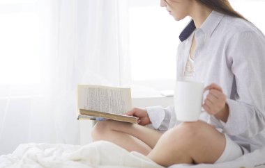 Yatakta oturup kitap okuyan ve kahvaltı yapan bir kadın.