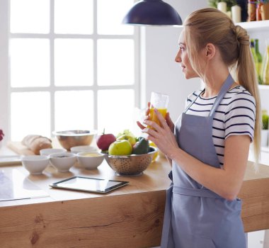 Çekici kadın mutfakta dikilirken elinde bir bardak portakal suyu tutuyor.