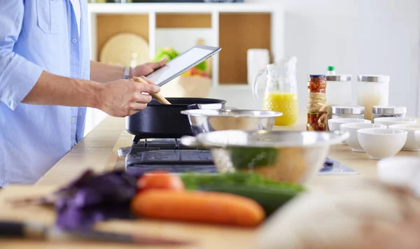 Man following recipe on digital tablet and cooking tasty and healthy food in kitchen at home — Stock Photo, Image