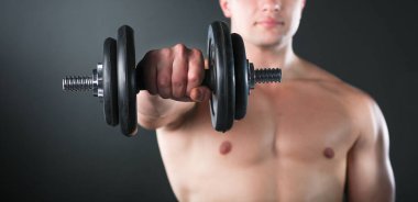 Siyah arka planda ağırlık kaldıran kaslı bir gencin yakın çekimi.