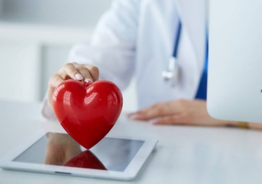 Steteskop tutan, kalbi hafif arka planda olan kadın bir doktor.