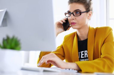 İş kadını ofiste bilgisayar ve cep telefonu kullanarak işine konsantre oluyor.