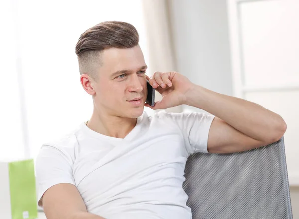 Bonito atraente sorrindo feliz alegre jovem do sexo masculino usando telefone e sentado na cadeira — Fotografia de Stock