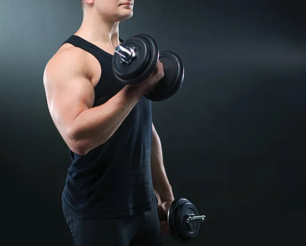 Primer plano de un joven musculoso levantando pesas sobre fondo oscuro — Foto de Stock