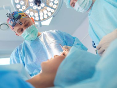 Ameliyat odasında arka planda erkek cerrah var.