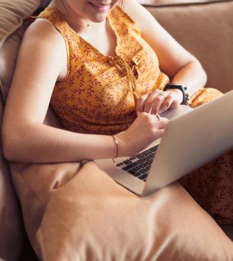 Evde dizüstü bilgisayar üzerinde çalışan kanepede oturan genç kadın