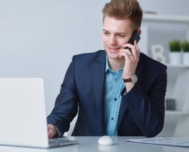 Yakışıklı genç adam dizüstü bilgisayarda oturuyor ve çalışıyor.