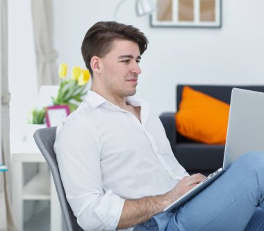 Yakışıklı genç adam dizüstü bilgisayarda oturuyor ve çalışıyor.