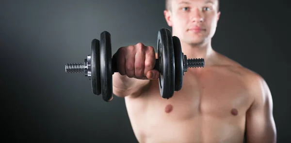 Primo piano di un giovane uomo muscoloso sollevare pesi su sfondo scuro — Foto Stock
