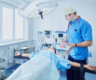 Ameliyat odasında arka planda erkek cerrah var.