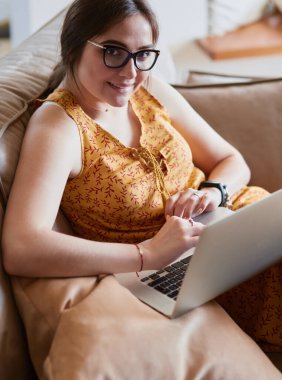 Evde dizüstü bilgisayar üzerinde çalışan kanepede oturan genç kadın