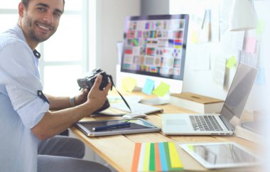 İnternette çalışırken bilgisayarın ve dizüstü bilgisayarın önünde grafik stüdyosunda oturan genç tasarımcının portresi.