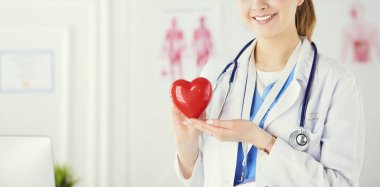 Steteskop tutan, kalbi hafif arka planda olan kadın bir doktor.