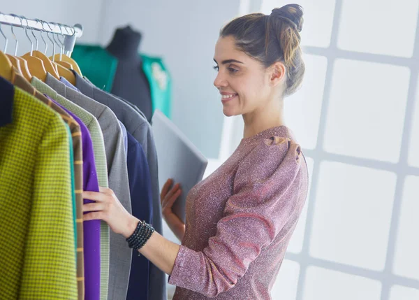 Schöne junge Stylistin in der Nähe von Gestell mit Kleiderbügeln — Stockfoto