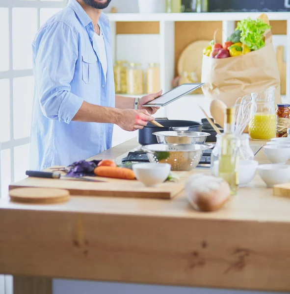 Hombre siguiendo la receta en la tableta digital y cocinar comida sabrosa y saludable en la cocina en casa —  Fotos de Stock