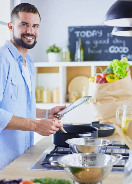 L'uomo segue la ricetta su tavoletta digitale e cucina cibo gustoso e sano in cucina a casa — Foto Stock