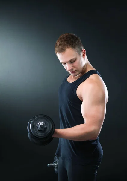 Nahaufnahme eines muskulösen jungen Mannes, der Gewichte auf dunklem Hintergrund stemmt — Stockfoto