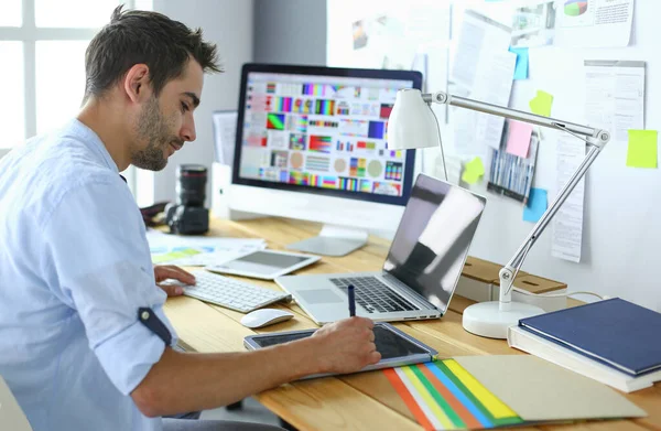 Porträt eines jungen Designers, der im Grafikstudio vor Laptop und Computer sitzt, während er online arbeitet. — Stockfoto