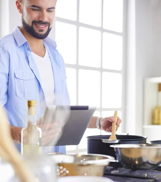 Hombre siguiendo la receta en la tableta digital y cocinar comida sabrosa y saludable en la cocina en casa — Foto de Stock