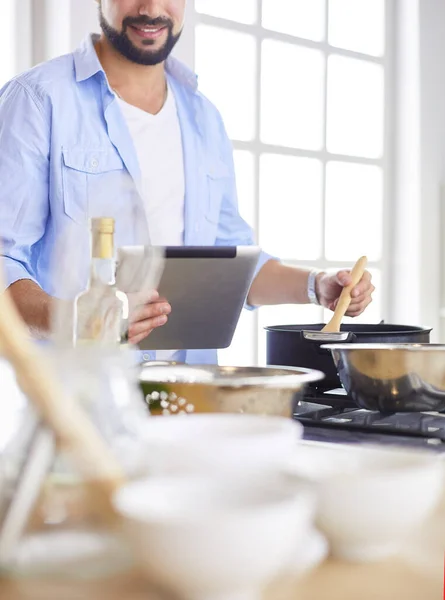 Man following recipe on digital tablet and cooking tasty and healthy food in kitchen at home — Stock Photo, Image