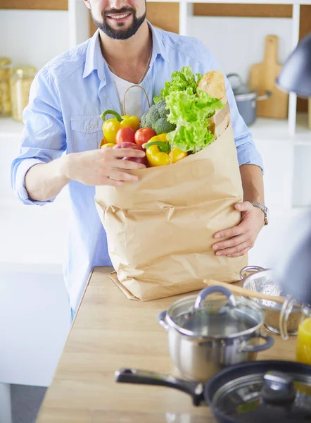 Mutfak arka planında poşet dolusu erzak tutan adam. Alışveriş ve sağlıklı gıda konsepti — Stok fotoğraf