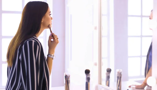 Mujer de belleza aplicando maquillaje. Hermosa chica mirando en el espejo y la aplicación de cosméticos con un cepillo grande — Foto de Stock