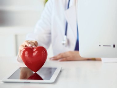 Steteskop tutan, kalbi hafif arka planda olan kadın bir doktor.