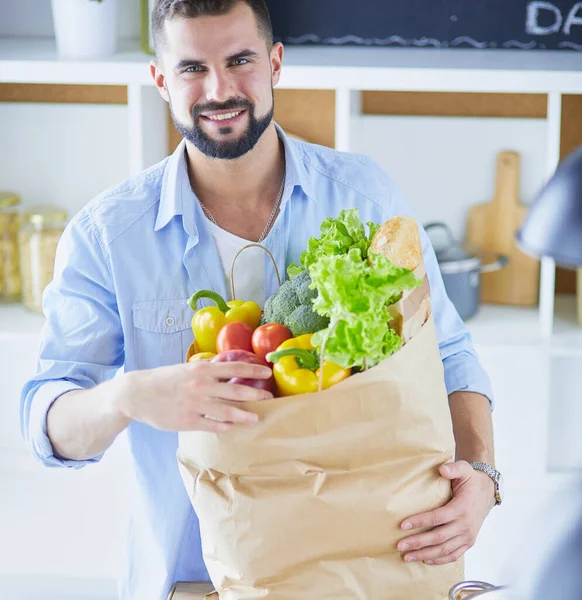 Man holding paper bag full of groceries on the kitchen background. Shopping and healthy food concept — Stock Photo, Image