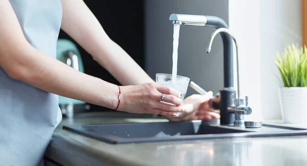 Mano umana che tiene il vetro che versa acqua fresca della bevanda al rubinetto della cucina — Foto Stock