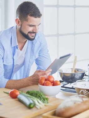 Dijital tablet ve yemek pişirme tarifine uyan bir adam evdeki mutfakta lezzetli ve sağlıklı yemekler pişiriyor.