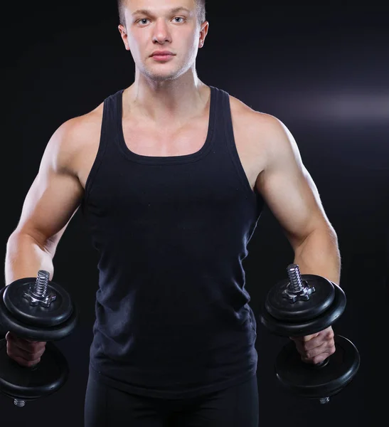 Primer plano de un joven musculoso levantando pesas sobre fondo oscuro —  Fotos de Stock