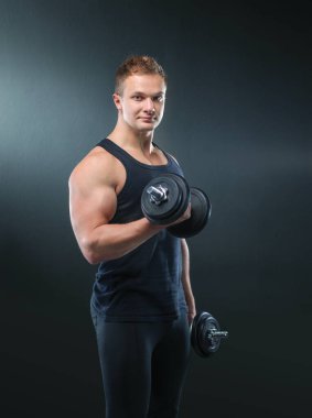 Siyah arka planda ağırlık kaldıran kaslı bir gencin yakın çekimi.
