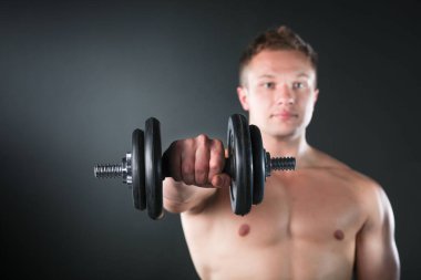 Siyah arka planda ağırlık kaldıran kaslı bir gencin yakın çekimi.